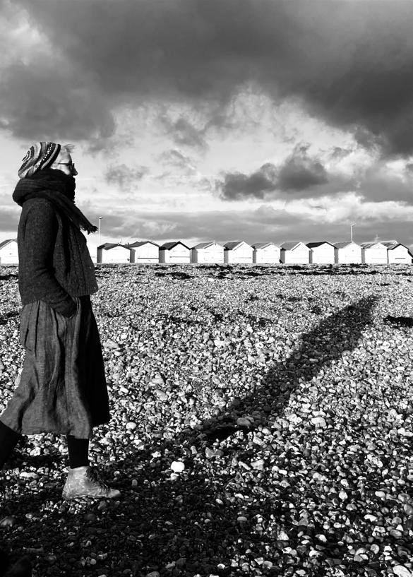 Black and white photograph of Sam walking on a pebbly beach